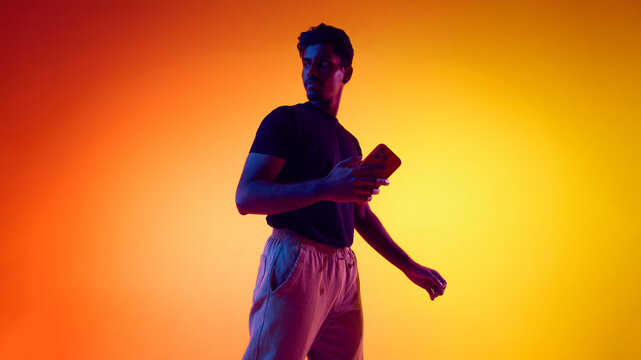 Man holding smartphone in dramatic colored studio lighting. Concept of consumer electronics promo, smartphone marketing visuals, product awareness campaign, and brand identity