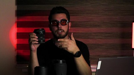 Man in dark studio showing camera lens and talking.