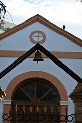 Pigeons flying over a shrine in Spain with a cross and a bell
