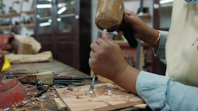 Close up of a carpenter using a chisel and mallet to carefully carve an intricate design into a wooden plank in a workshop, Siem Reap, Cambodia.