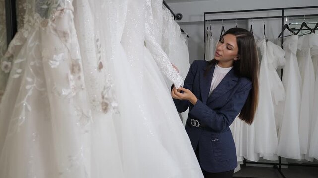 A stunning bride selects a wedding gown in a bridal boutique. The gowns are displayed on racks, a plethora of options. Preparations for the nuptials.