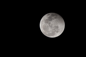 A bright full moon with visible craters shines as a glowing lunar sphere against the dark black void of the night sky in the deep universe