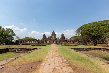 The ancient stone architecture of Phimai Castle stands majestically against the summer sky, amidst the ruins of old temples and the lush green meadows of the Nakhon Ratchasima countryside, Thailand.