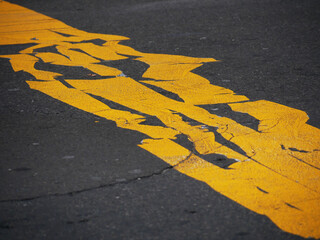 thick and broad aged and misaligned yellow painted lines on a tarmac street 