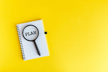 Magnifying glass on notebook with word PLAN on yellow background, concept of planning and organization. © Татьяна Зернова