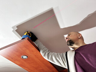 Man installing a wooden shelf using a laser level tool indoors during home renovation