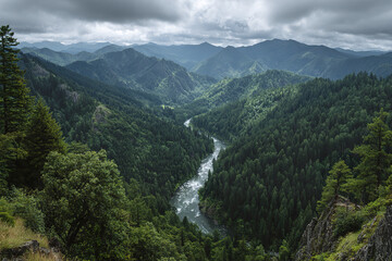 Fototapeta premium Rolling forested mountains with river valley scenic natural landscape under cloudy sky, peaceful wilderness with dense green trees and flowing water in remote area