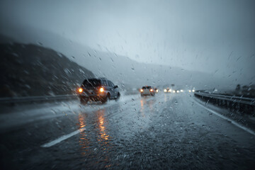 Fototapeta premium Rainstorm on highway with wet road and cars driving in severe weather conditions, creating reflections and moody atmosphere during low visibility