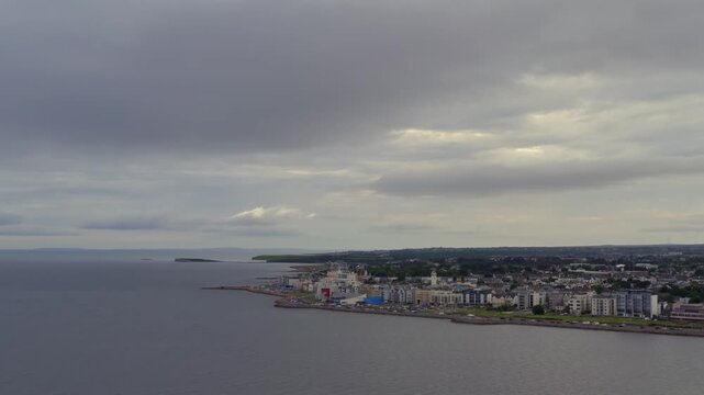 Aerial dolly shot revealing Salthill village along Galway Bay, with expansive seascape and city coastline under dramatic skies