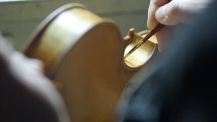 Artisan antiquing a new violin with careful hand applied varnish techniques for a vintage aged appearance and aesthetic.