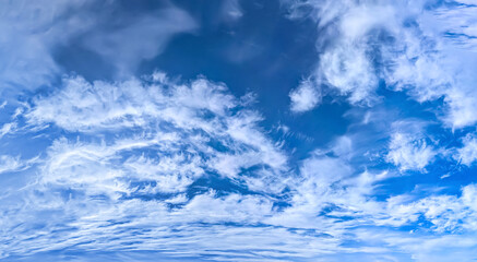 A panorama of cumulus clouds against a blue sky. A summery, serene landscape. The cloud's smooth movement copy space for banner text. Clear background with tiny white fluffy cloud.
