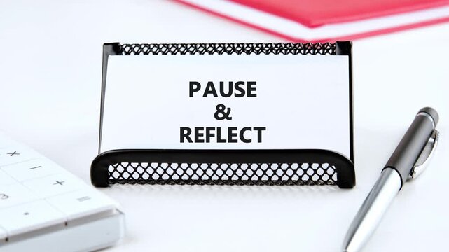 Message unfolds from scribbles to a crisp PAUSE  REFLECT on a small whiteboard, beside a silver pen and red book, promoting mindfulness and introspection