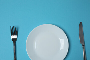 Empty plate and cutlery on colored background, top view
