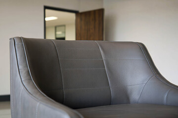 Close-up of a textured gray leather chair with detailed stitching in a minimalist interior. Neutral wall and doorway in the background.
