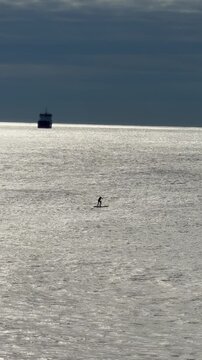 Minimal paddle surfer alone on endless calm sea under dramatic cloudy sky, abstract seascape resembling a desert, solitude and freedom concept, cinematic ocean landscape with copy space and surreal at