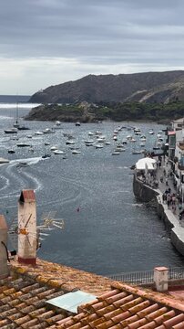 Panoramic panning shot of Costa Brava coastal village harbor with boats and yachts on calm Mediterranean sea, scenic summer travel destination with coastline, bay, marina and seaside town atmosphere