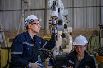 Blue collar workers are working at machine shop with welding robot arm.