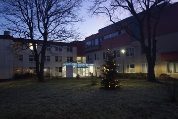 Beleuchtetes Krankenhausgel&auml;nder mit Christbaum auf Wiese bei Frost und K&auml;lte in der Nacht im Winter