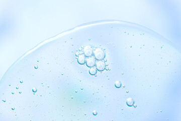 Macro close-up of a single cluster of small transparent bubbles suspended in clear liquid with soft blue tint, smooth curved surface and refraction creating fresh clean cosmetic texture. Copy space