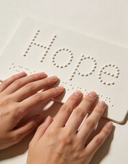 Hands gently sliding over Braille letters forming the word &ldquo;Hope&rdquo; on a neutral minimal background, symbolizing accessibility, literacy, inclusion, and awareness concept