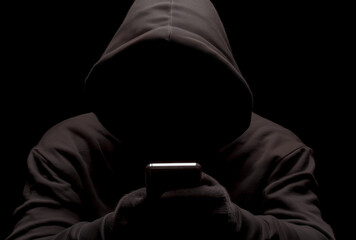 a hacker in a black hoodie holding a mobile phone