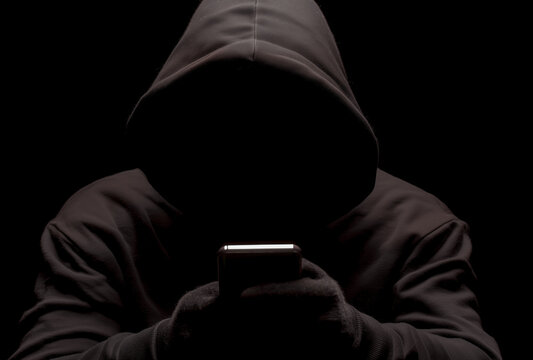  a hacker in a black hoodie holding a mobile phone