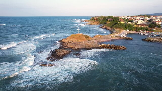 Aerial view of the white cross standing tall on the rocky coast, contrasting with the blue waters and the town in the background, Lozenets, Tsarevo, Bulgaria.