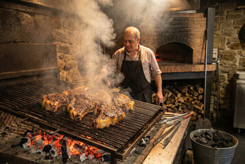 Maestro parrillero cocinando chuletas a la brasa en cocina r&uacute;stica