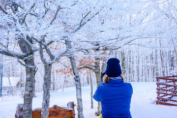 A nordic skier pauses on a trail to take a smartphone photo of trees covered in thick white hoarfrost near Collingwood, Ontario, highlighting technology in nature.