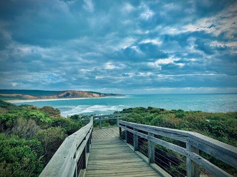 Wooden boardwalk leading to ocean under dramatic cloudy sky
