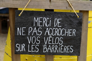 Merci de ne pas accrocher vos v&eacute;los sur les barri&egrave;res. Inscription blanche sur grande ardoise noire.