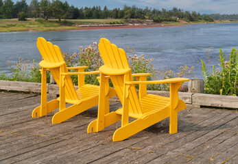 A pair of Adirondack chairs on a wooden deck overlooking the sea.