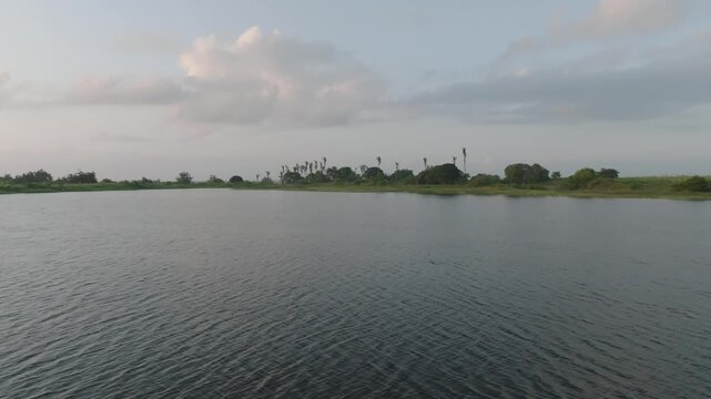 Aerial view of a serene lake reflecting the sky, bordered by lush green vegetation and scattered trees, Kwale, Kwale County, Kenya.