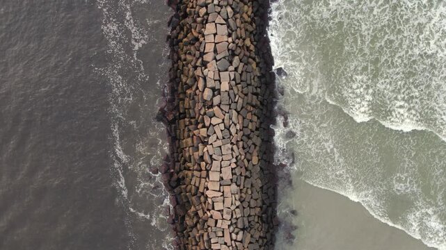 Aerial view of a dark rock jetty slicing through the contrasting ocean, where dark and light waters collide in Wells, Maine, United States.
