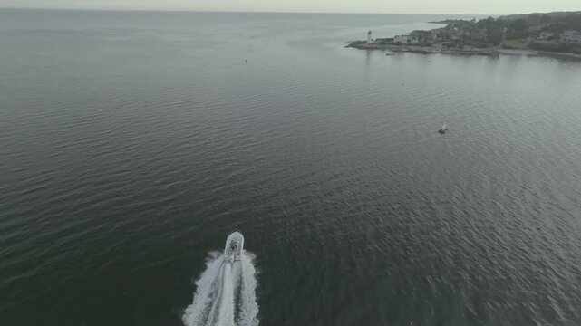 Aerial view of a boat slicing through the serene waters near Eastern Point Light, contrasting with the coastline, Gloucester, Massachusetts, United States.