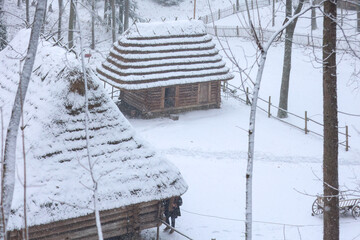Traditional wooden houses with thatched roofs in a snowy winter landscape. Shevchenko Grove, Lviv, Ukraine