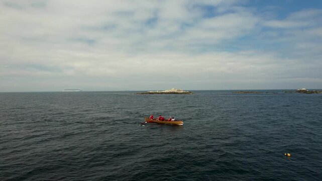 Aerial view of a small boat with people in red, traversing the dark blue waters near Dalkey Island, under a cloudy sky, Dalkey, County Dublin, Ireland.