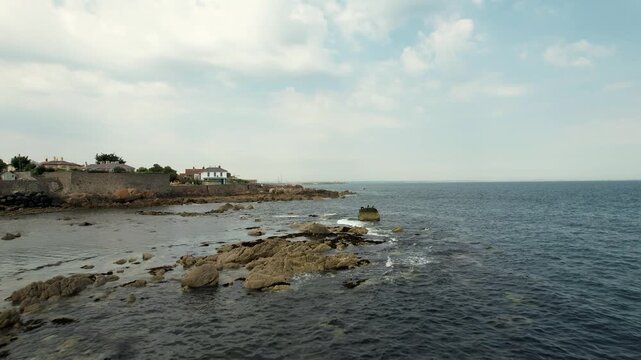 Aerial view of a rugged, rocky shore with buildings standing prominently against the backdrop of the expansive ocean, Dalkey, County Dublin, Ireland.