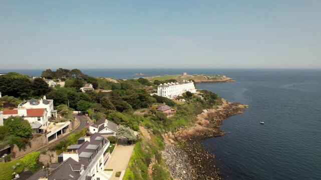 Aerial view of Dalkey Island's lush greenery meets the deep blue sea, contrasted against the white buildings along the rocky coastline, Dalkey, County Dublin, Ireland.
