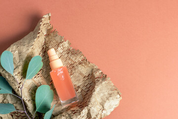 Cosmetic spray bottle with coral liquid on textured paper and eucalyptus leaves on orange background. Top view, flat lay, copy space
