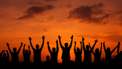 Silhouette of people raising hands against a vibrant sunset sky.