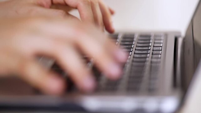 Person typing on a laptop keyboard with both hands in a bright environment