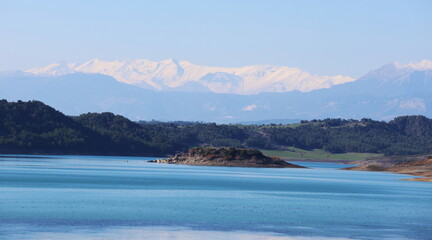 Breathtaking panoramic view of a deep blue lake surrounded by pine forests and snowy mountain peaks