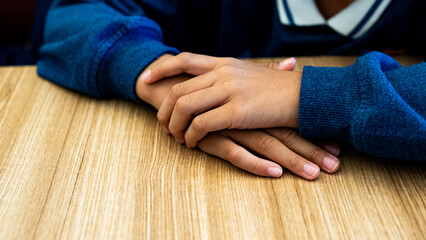 A detailed shot of a child's hands clasped together on a light-colored wooden table, representing focus, patience, and the educational environment.