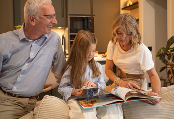 Grandparents and granddaughter enjoy family bonding while reading a book on the couch