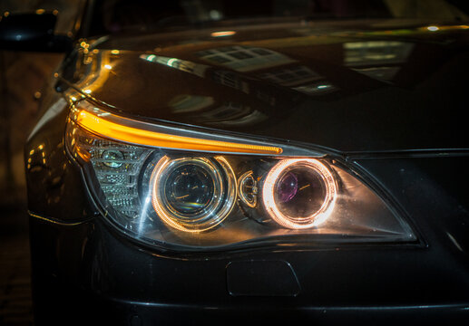 BI-LED headlights of a modern and expensive black car, hood and radiator grille. Front BI-LED headlight on a black SUV car. Glossy black premium car BI-LED headlights close-up. Angel eyes headlight. 
