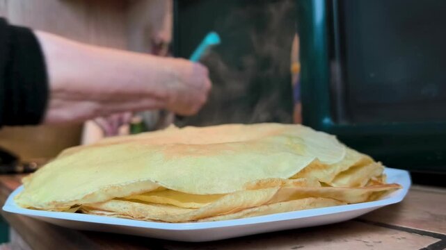 Stack of crepes in focus with a person cooking in background.