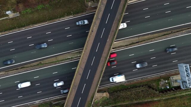 Aerial view of multiple cars speeding along a dark gray highway intersected by a light gray overpass, Milton Keynes, England, United Kingdom.