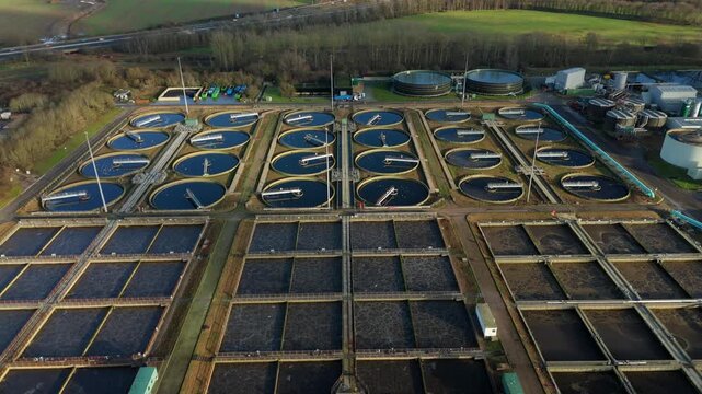 Aerial view of circular and square tanks at a water treatment facility with surrounding green spaces, Milton Keynes, England, United Kingdom.