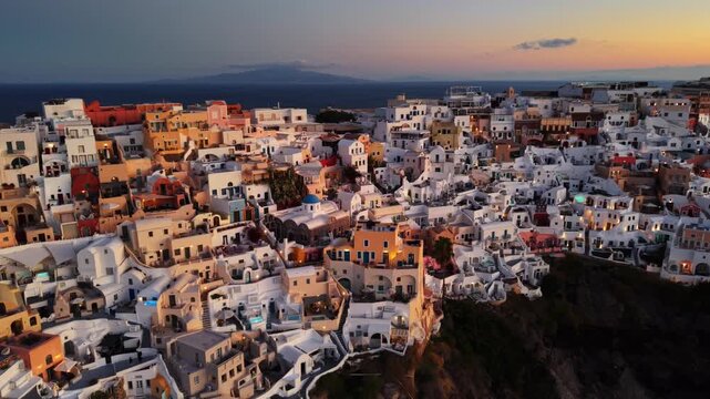 Aerial view of the iconic white buildings cascading down the cliffs of Oia, bathed in the warm glow of sunset, creating a mesmerizing contrast, Oia, Thira, Greece.